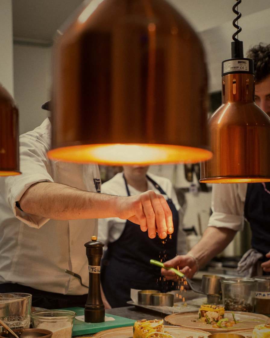 Nella cucina di un ristorante, sotto le lampade di rame, gli chef rifiniscono i piatti prima del servizio